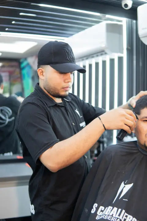 Barbero con gorra haciendo un corte con máquina
